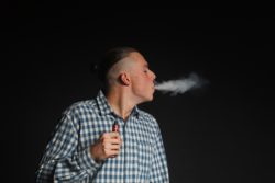 Young man exhales vaping cloud 