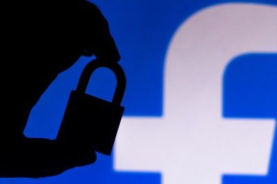 Silhouette of hand holding padlock in front of Facebook logo - Facebook privacy