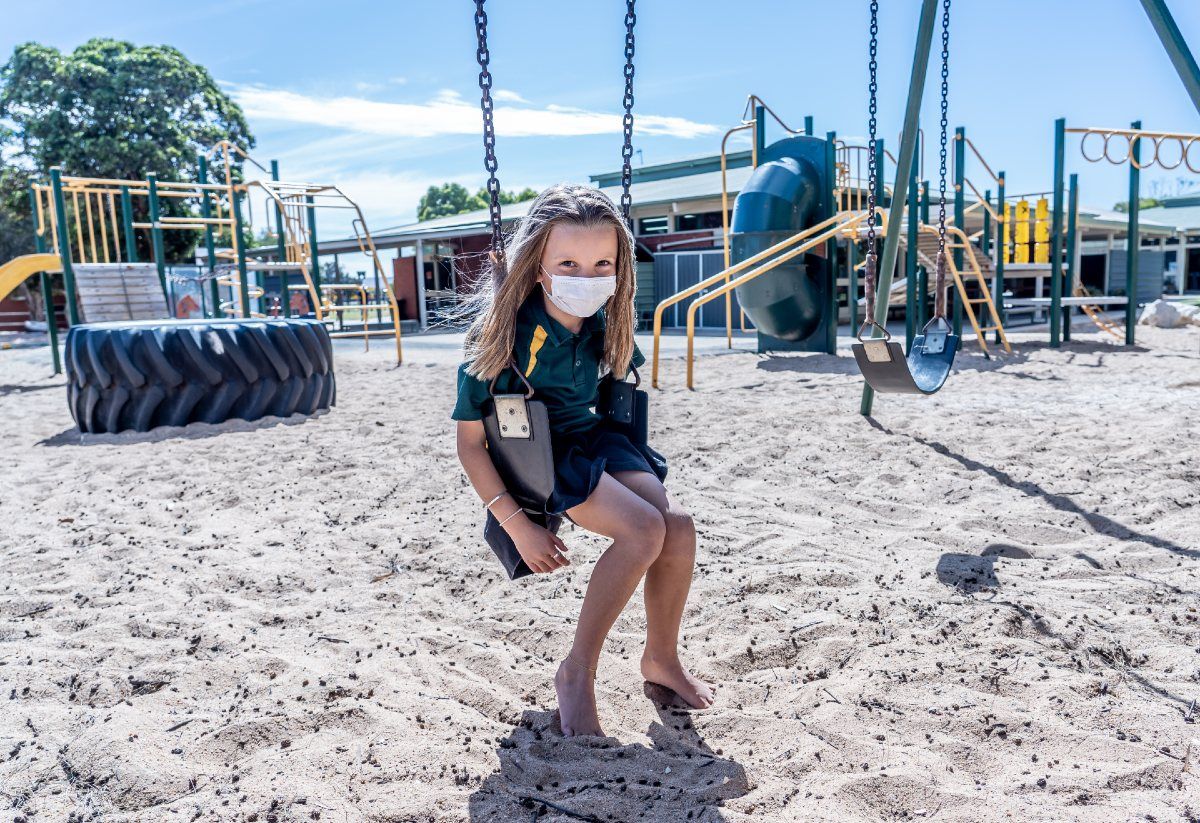 A young girl wearing a face mask sits alone on a swing set - Florida education