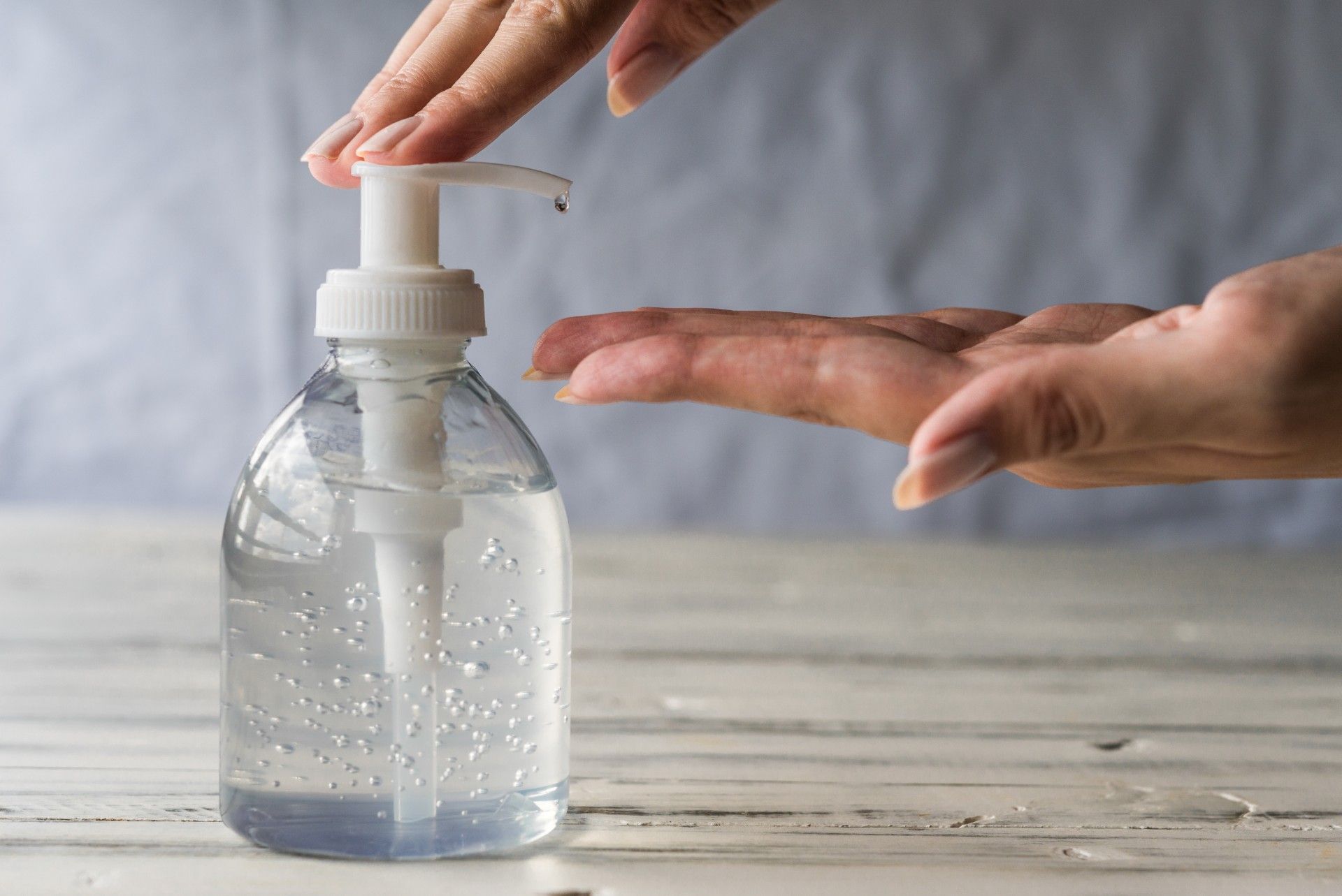 Person dispenses clear hand sanitizer from a pump bottle onto their hand 