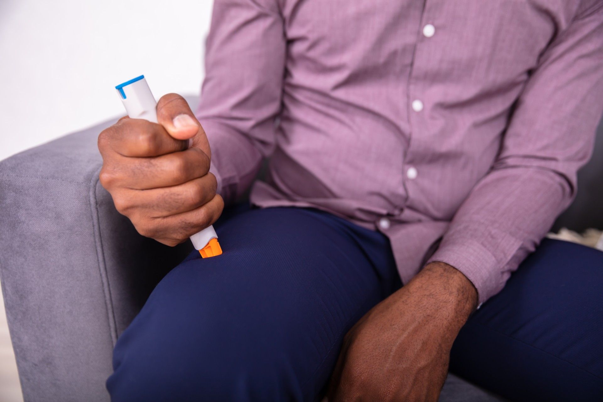 Seated man injecting himself in the thigh using an EpiPen
