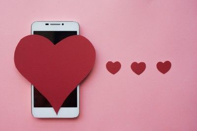 Large, red heart sitting over screen of smartphone next three smaller hearts on pink background - zoosk app