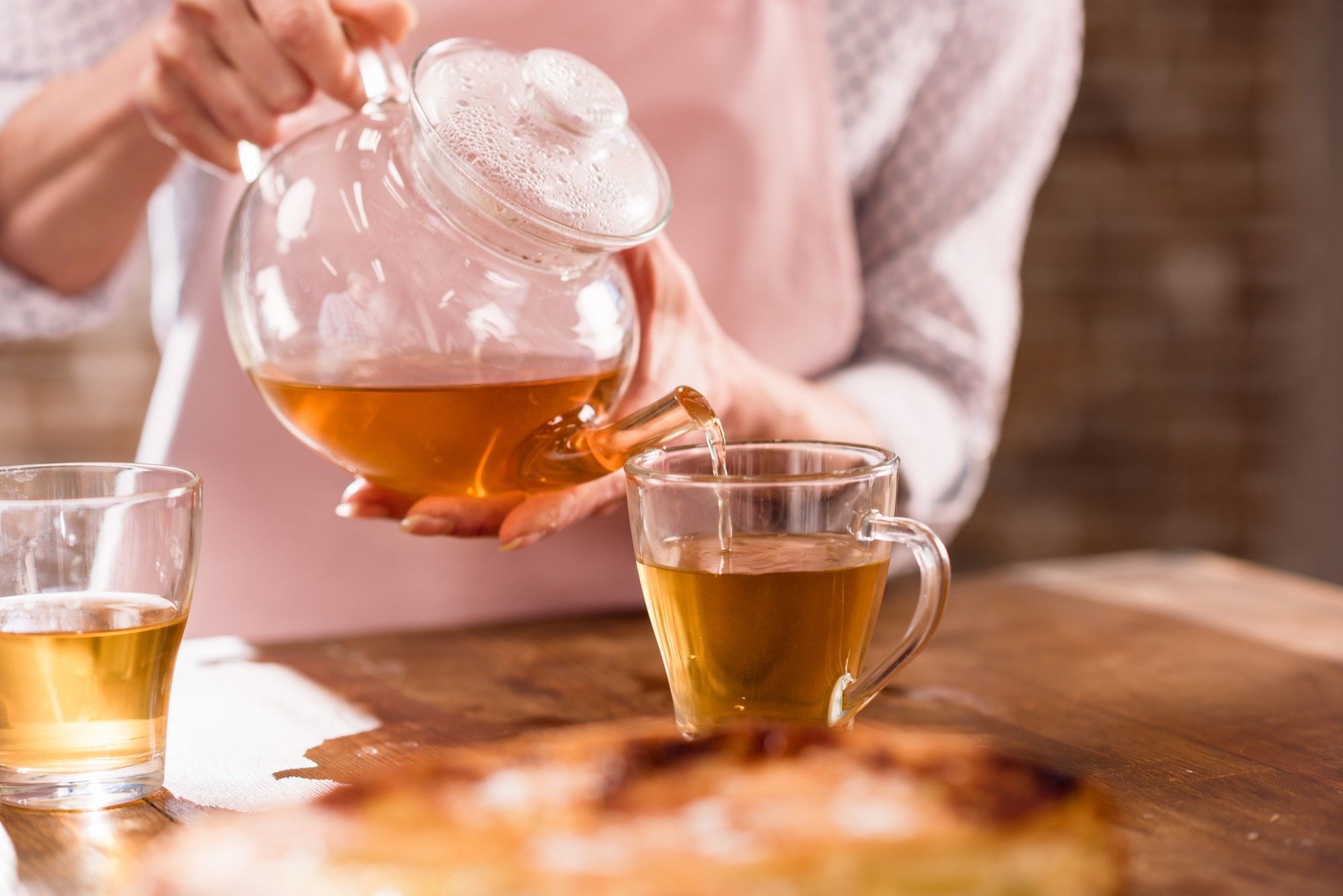 Woman pours Bigelow tea from glass teapot.