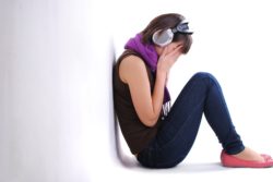 Depressed teen girl sits against wall with headphones on and head in hands