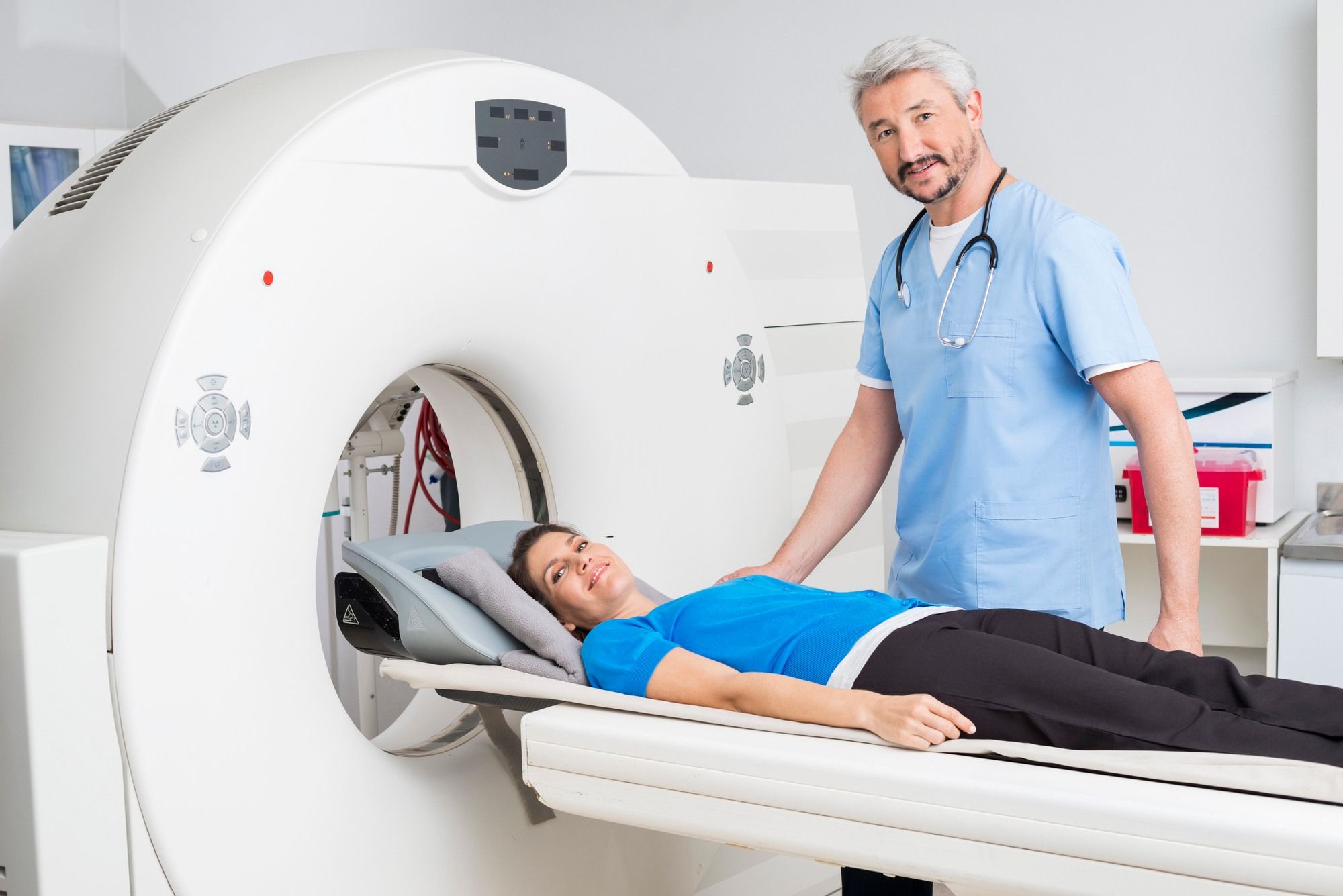 Male doctor stands next to female patient who is on MRI machine