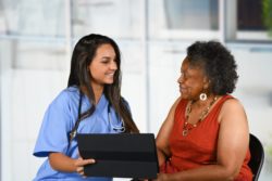 Female nurse counsels elderly female patient with laptop