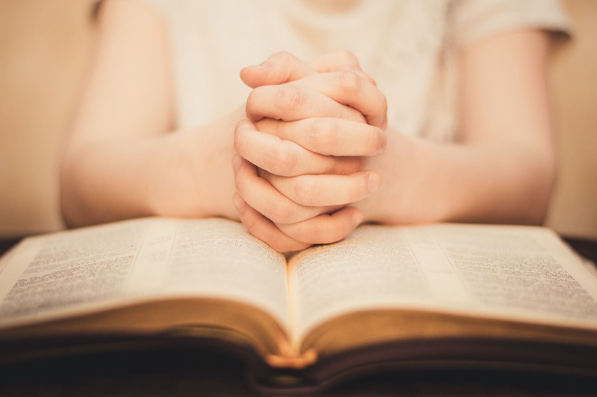 Closeup of young girl's clasped hands on open Bible