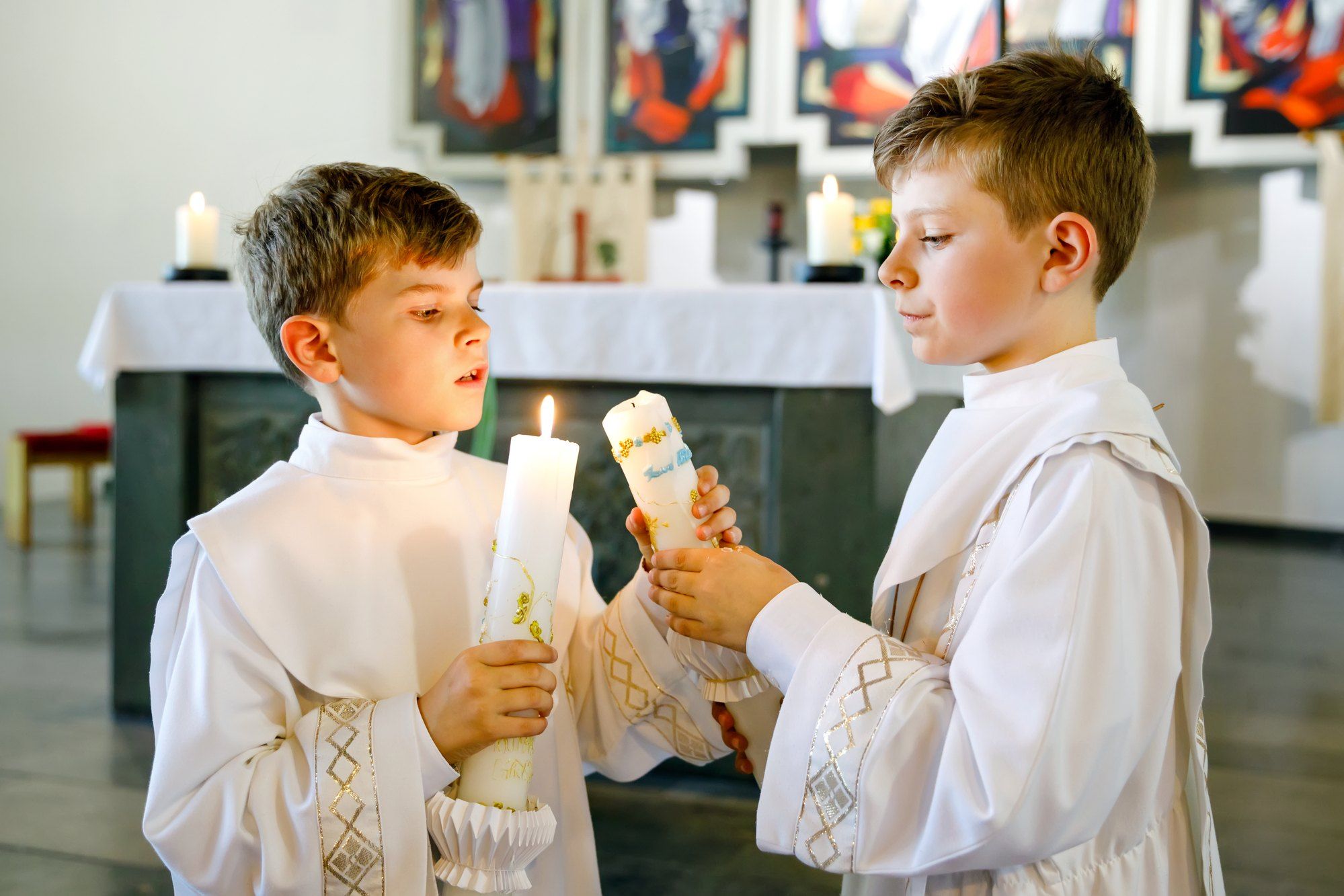 Two boys in white gowns light candles at church