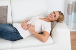 Woman lays down on couch holding her stomach in pain