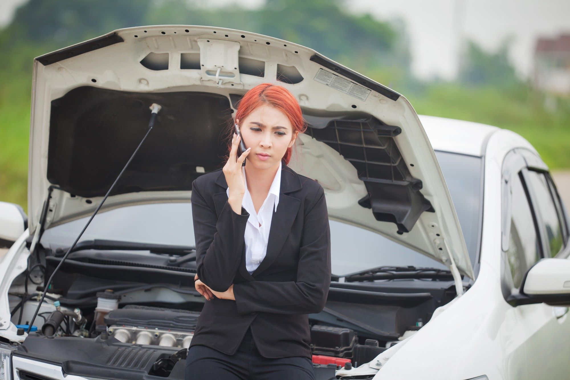 Young woman stands in front of broken down car