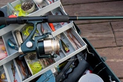 Tackle box contains bait and other fishing gear, with reeled fishing pole lying across the top - Pure Fishing