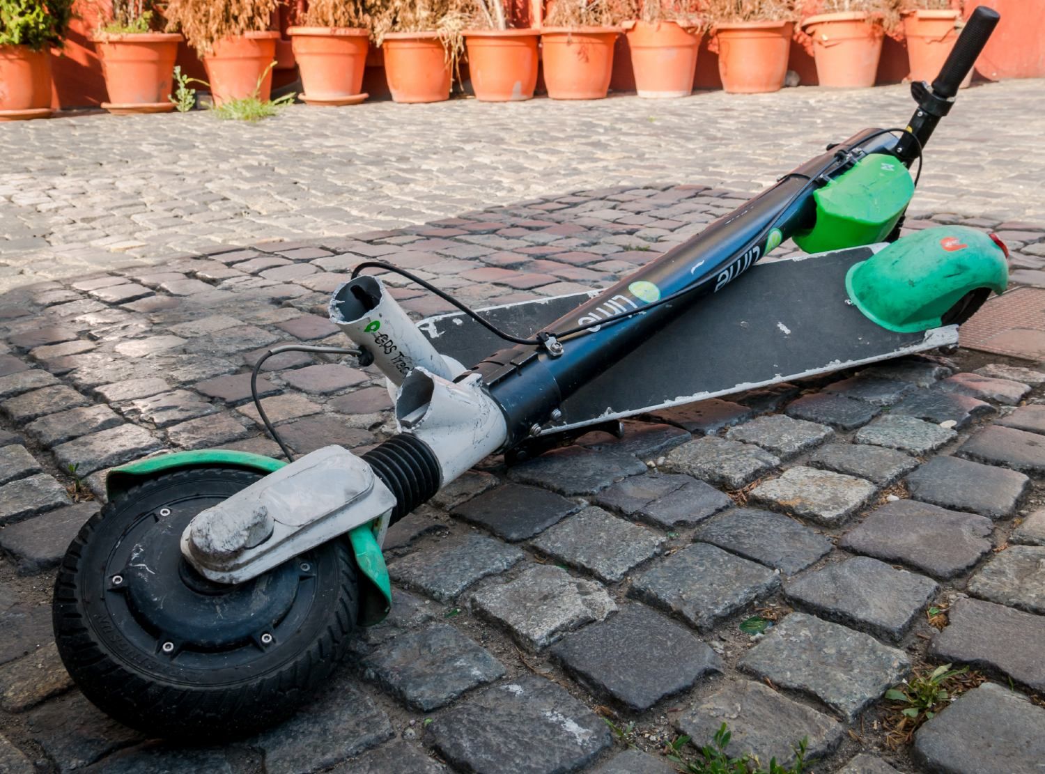 A broken Lime electric scooter lies on a stone path - Lime scooter rental