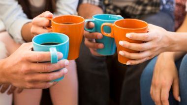 Four people hold orange and blue mugs of coffee close together - Maxwell House