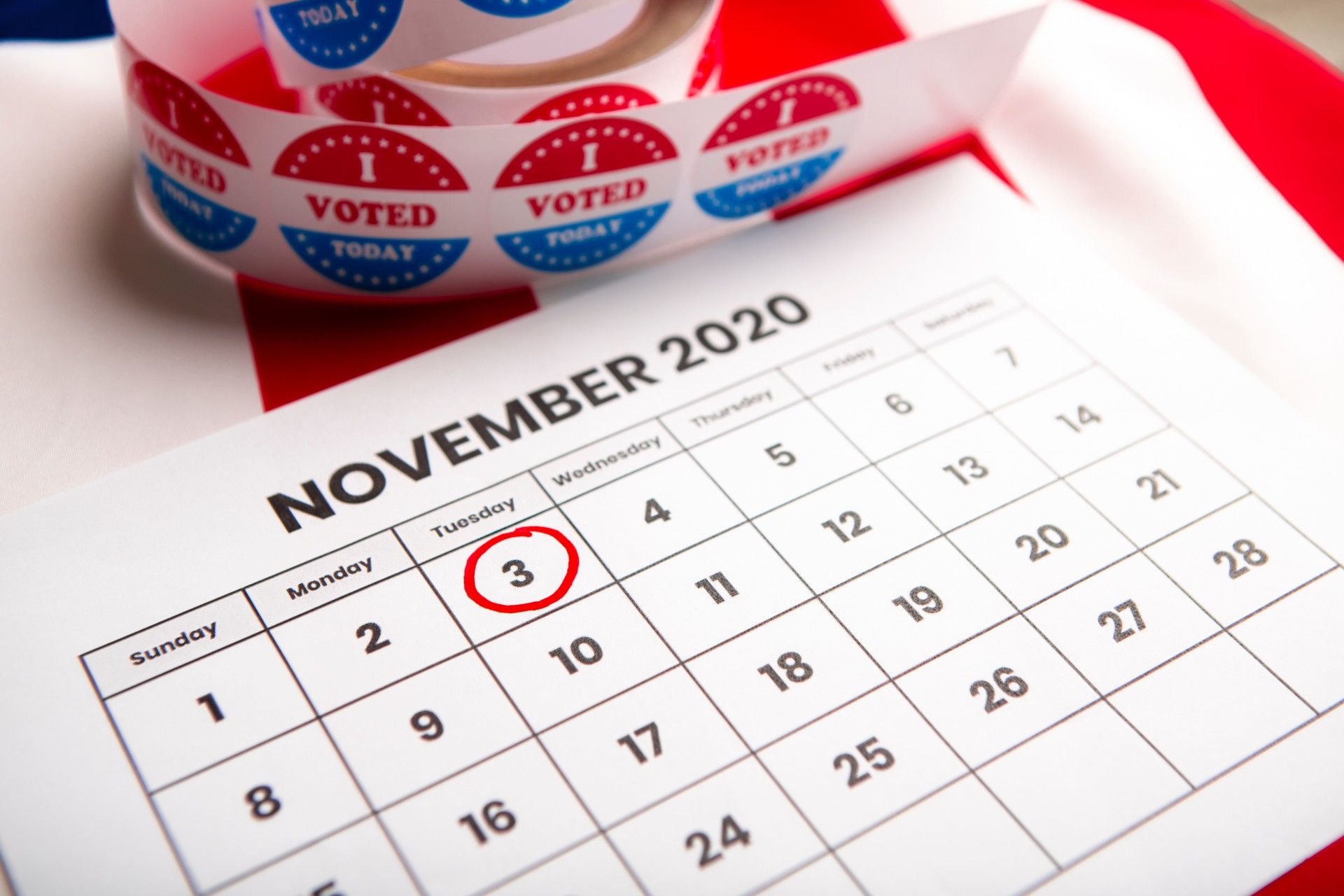 A roll of red-white-and-blue "I voted today" stickers sitting near a November 2020 calendar with the 3rd circled in red - Illinois voters