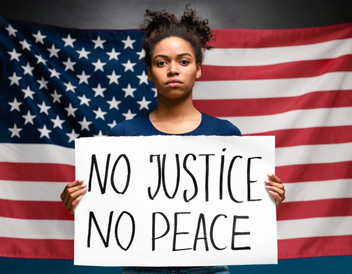 woman holding no justice no peace sign to seek racial justice