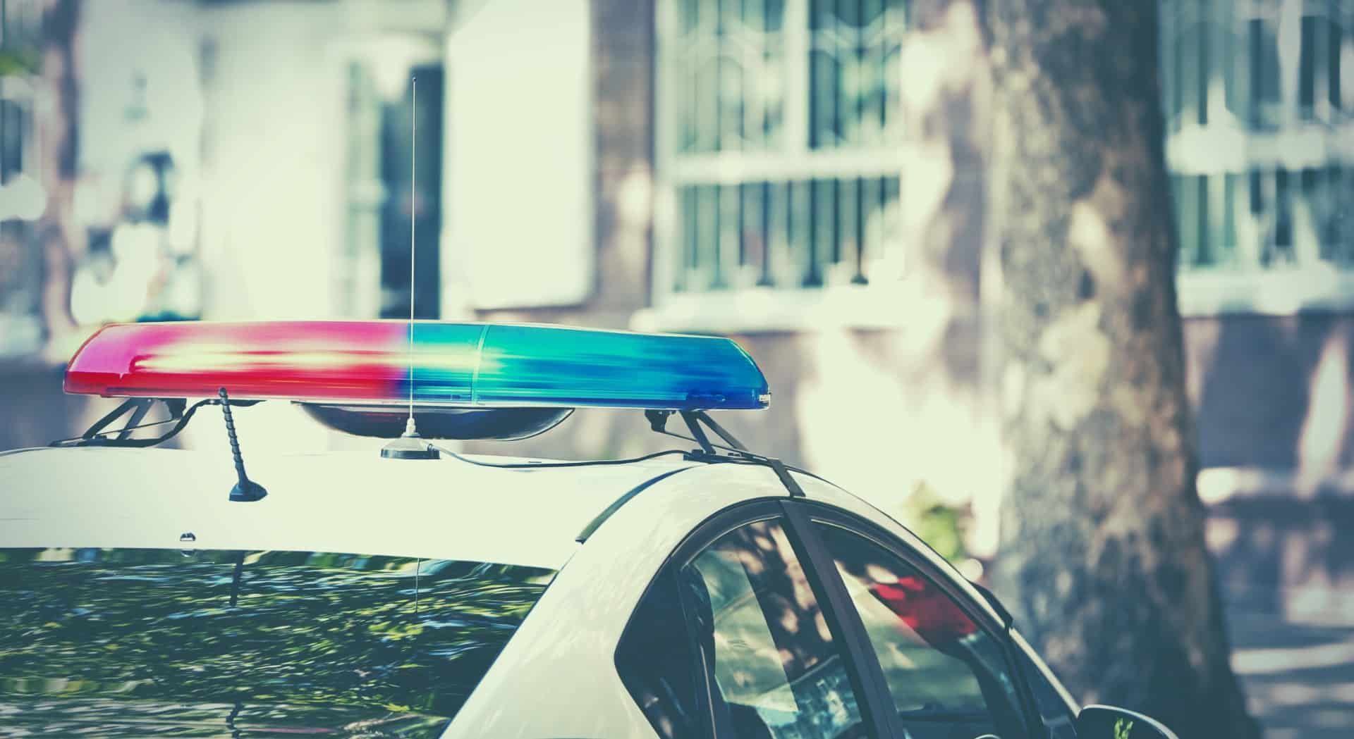 A police cruiser with lights on is parked on a residential street during daytime - police brutality