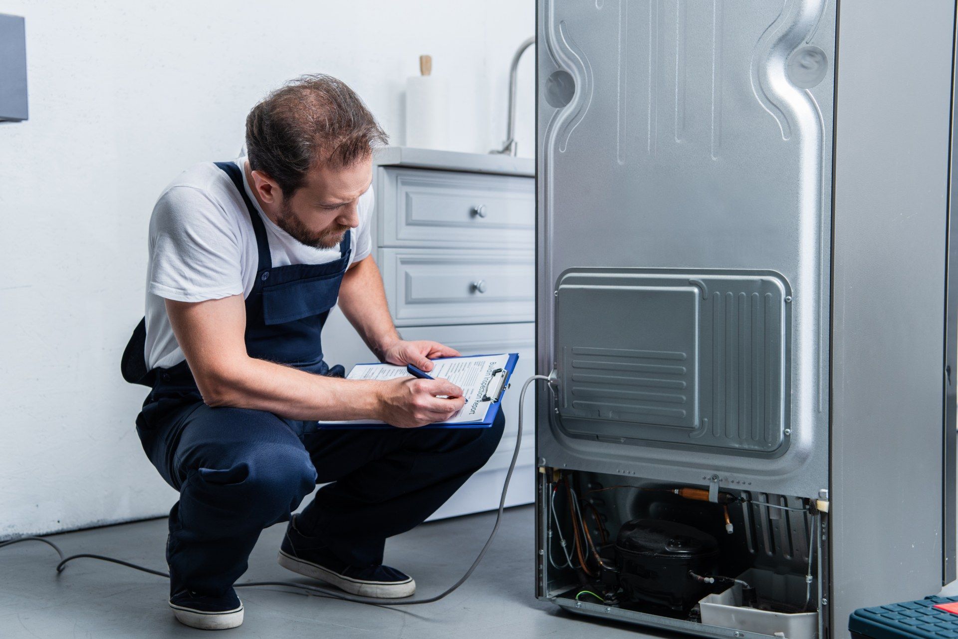 Repair technician works on the back of a silver refrigerator in a kitchen - lg electronics refrigerators