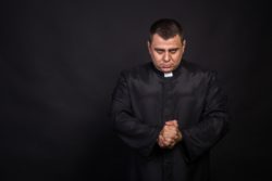 Serious priest with hands clasped in front of him