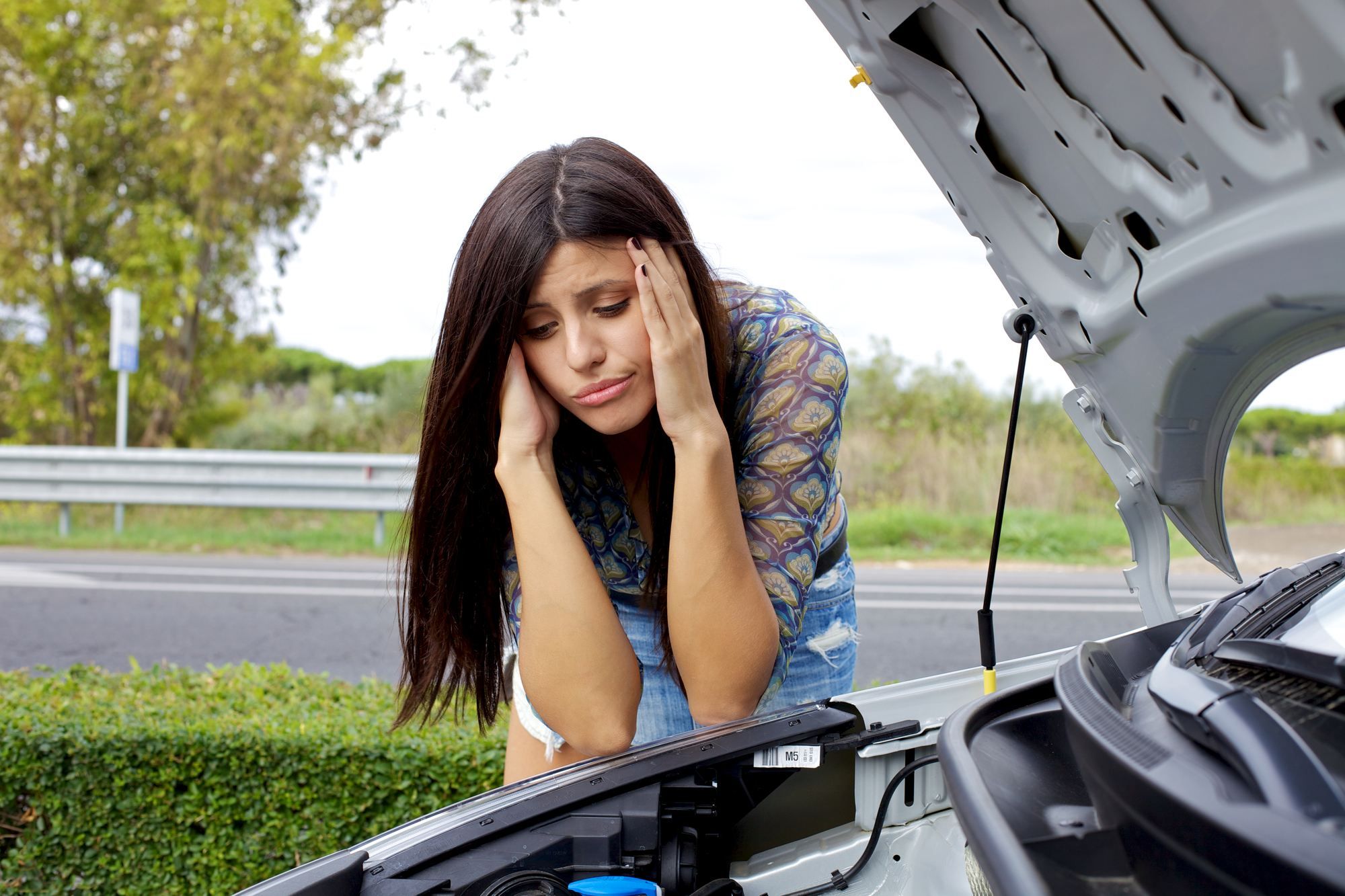 woman looking at engine of broken-down car