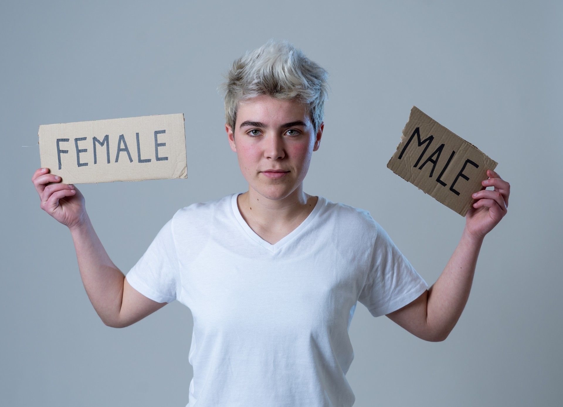 Transgender teen in white t-shirt holds up words "female" and "male" written on cardboard