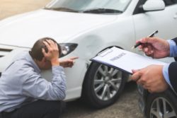 upset man points to car's damage while adjuster writes on pad and paper