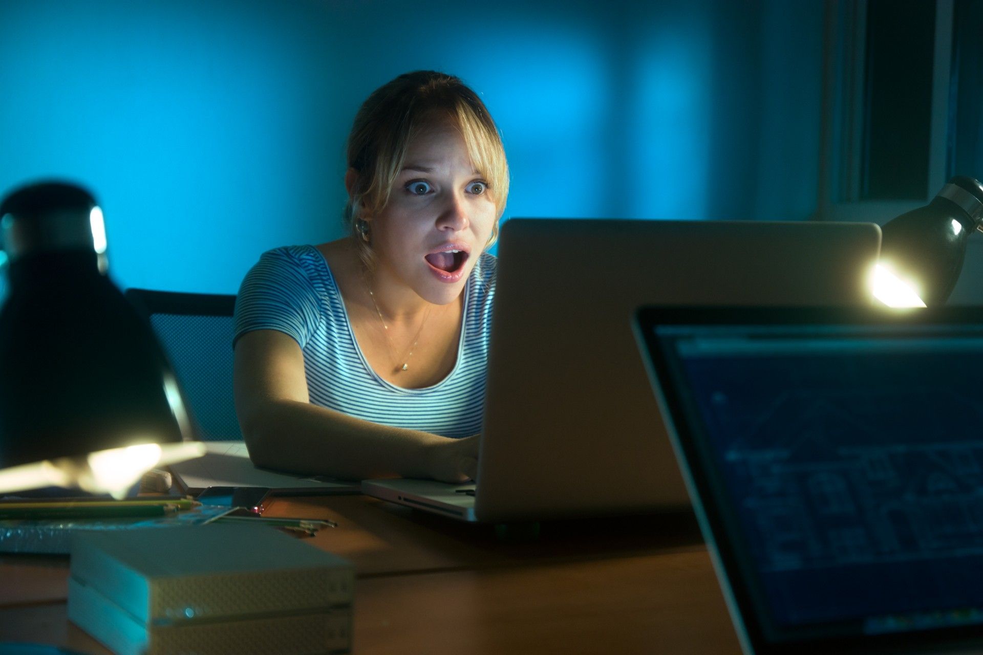 Woman working on laptop at night looks shocked at what she sees on the monitor - ASU