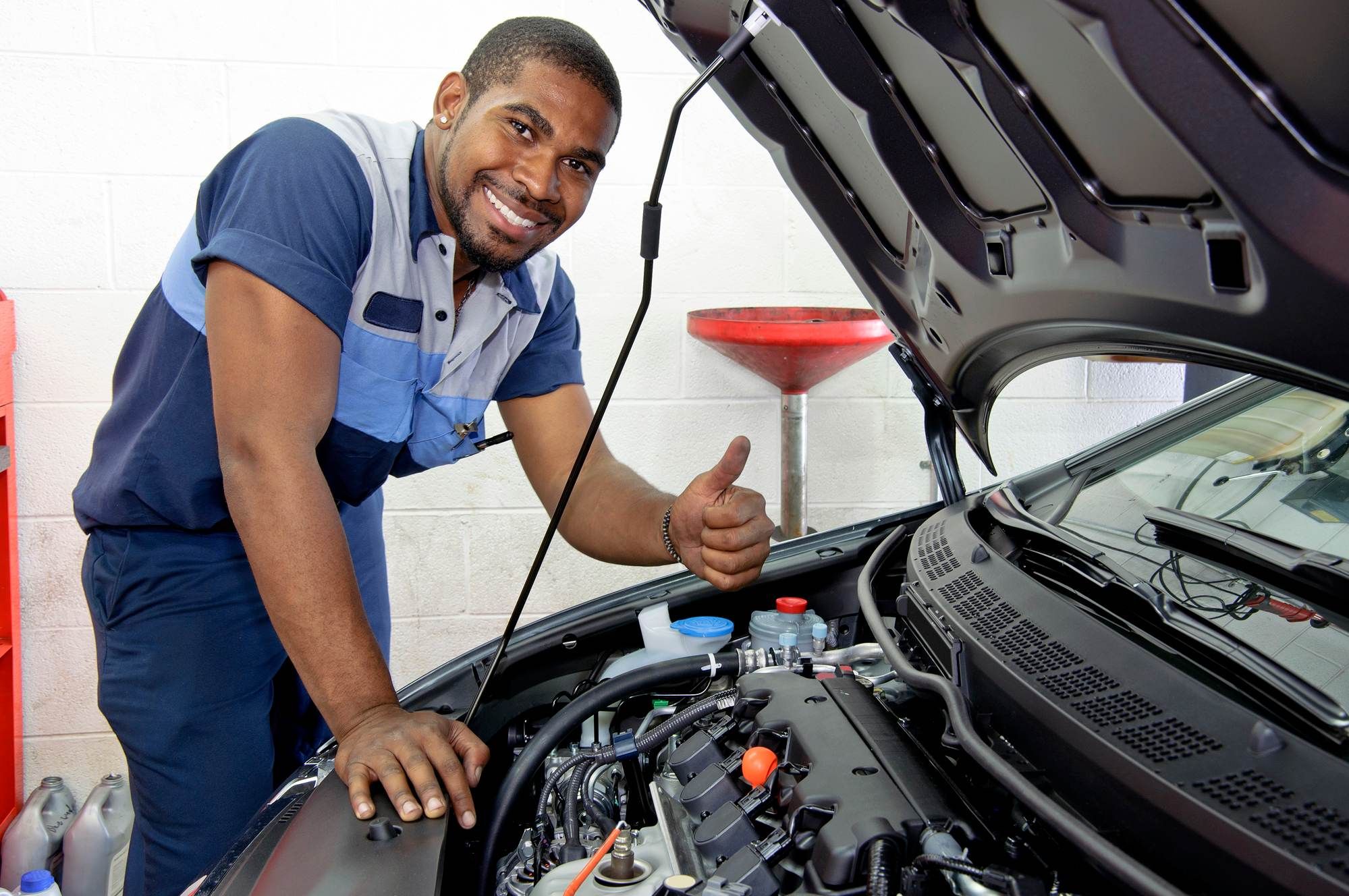 Auto technician gives a thumbs up as he works under hood of a car