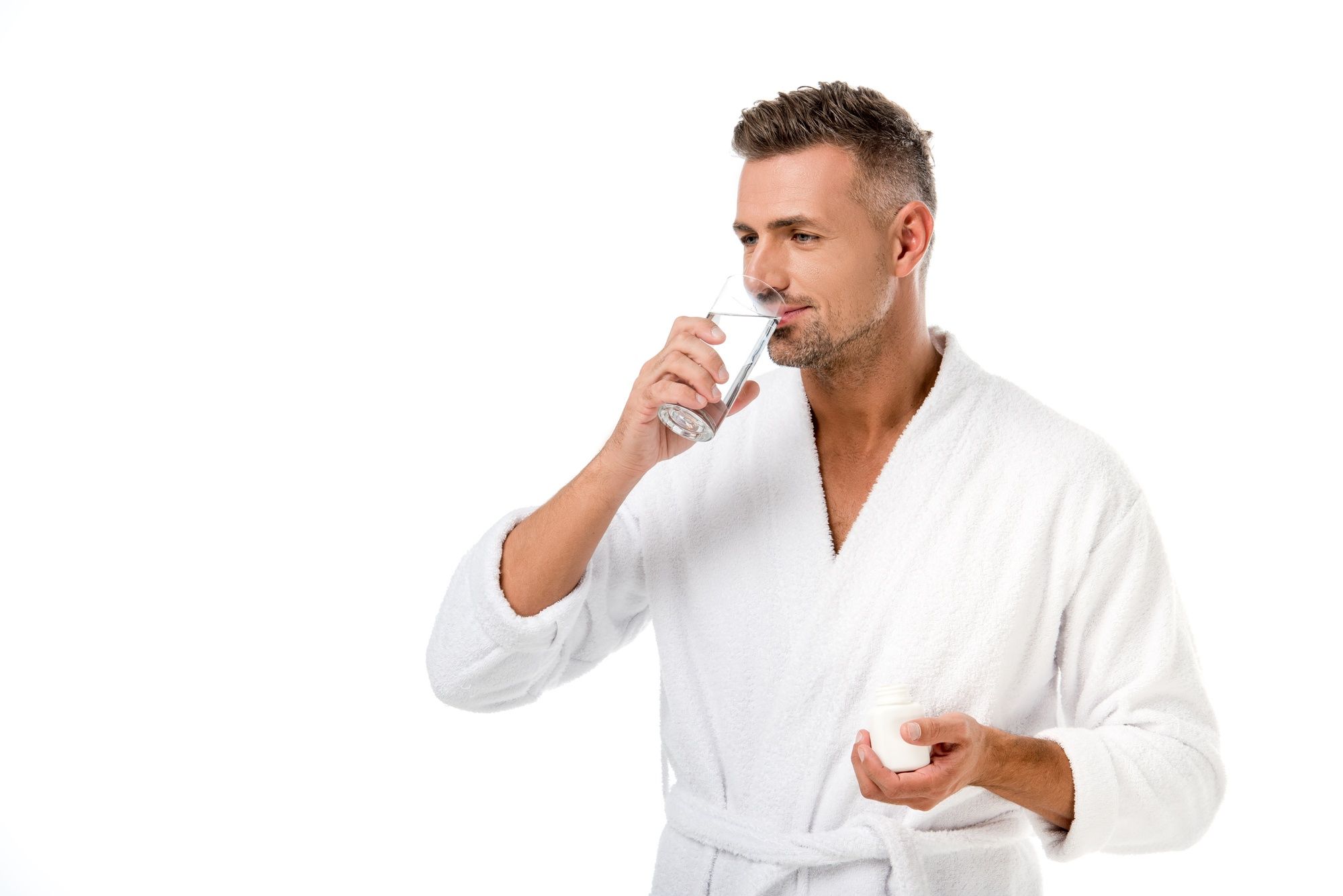 Man in white bath robe takes pills with glass of water