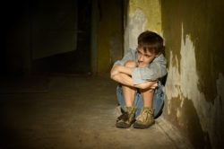 Scared boy huddled against wall in dark cellar