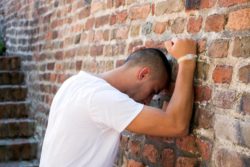 Upset older teen leans against brick wall