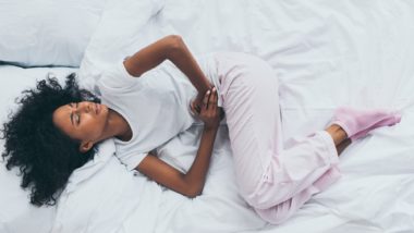 Woman suffering abdominal pain lies on bed