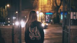 Woman with backpack walks towards street at night