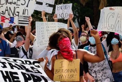A Black woman in a mask wears a sign that reads "I am Breonna Taylor" while participating in a protest - Breonna Taylor's death