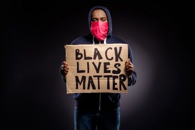 Black man in black hoodie and red face mask holds "Black Lives Matter" sign - police brutality BLM protesters