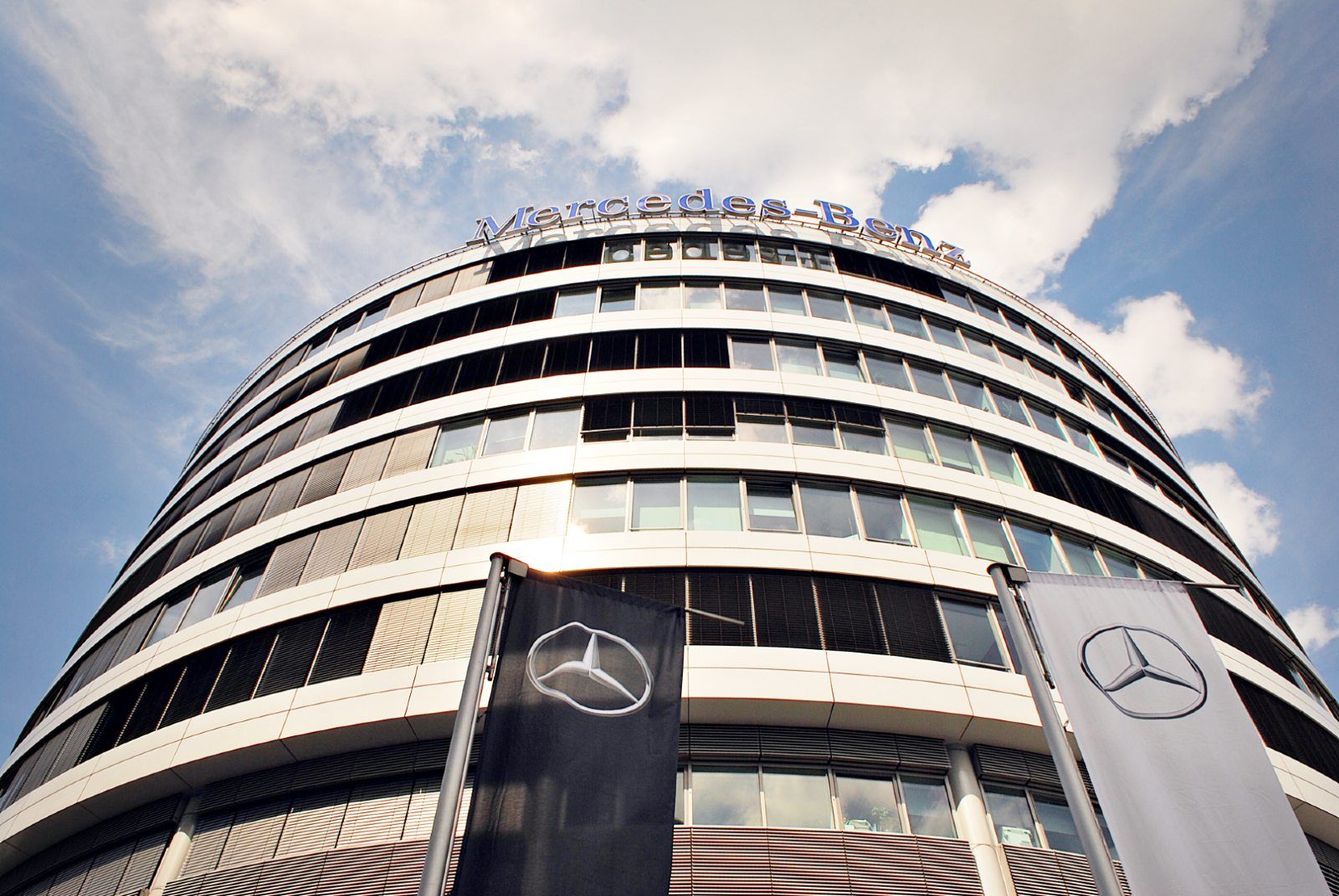 Flags with Mercedes-Benz logos stand in front of a large Mercedes-Benz office building - Mercedes bluetec