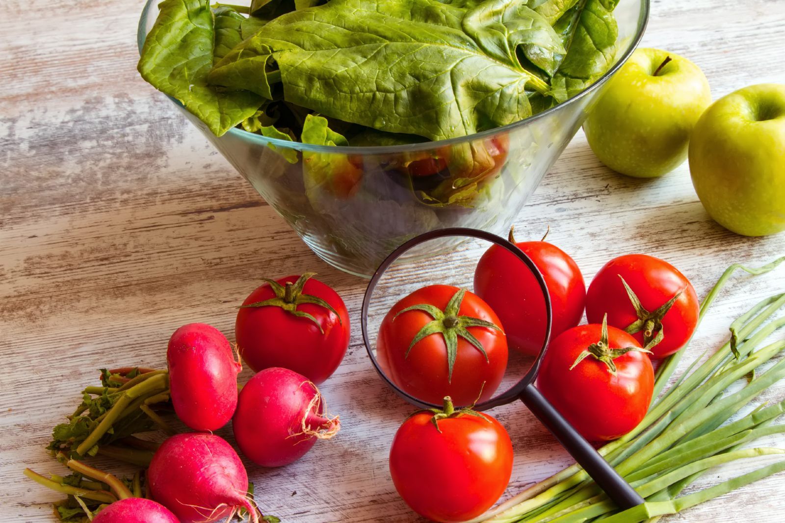 Produce sits in and near a glass bowl, with a magnifying glass lying on top of tomatoes - chemicals in food
