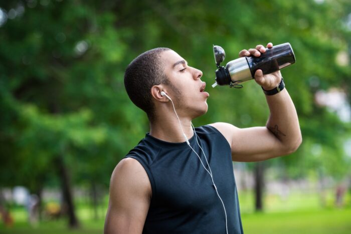 young african american sportsman drinking water from sports bottle in park