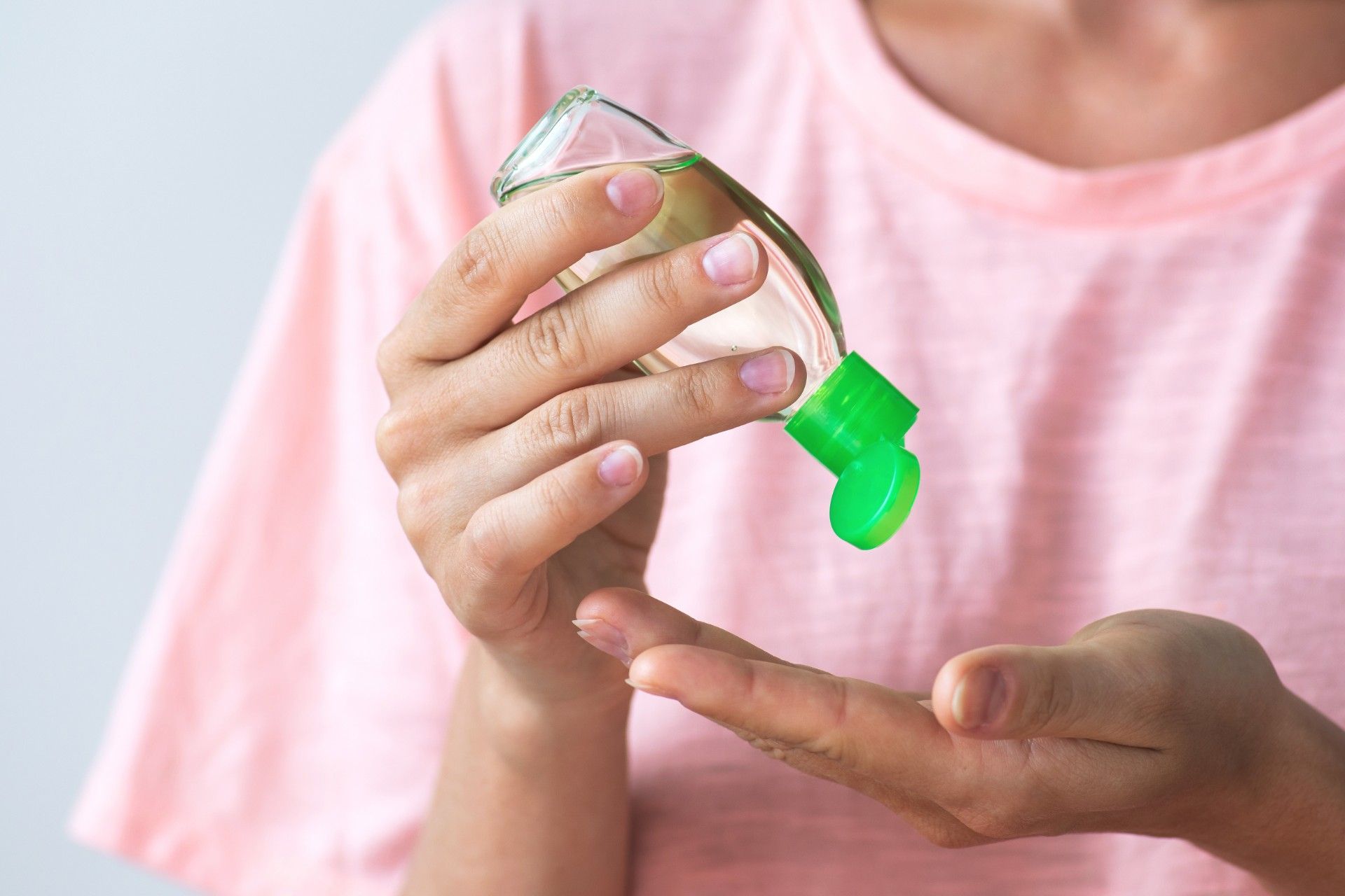 A woman dispenses hand sanitizer into her hand from a bottle with a green cap
