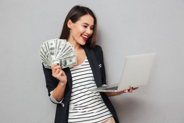 woman holding computer and cash she got from filing for class action rebates