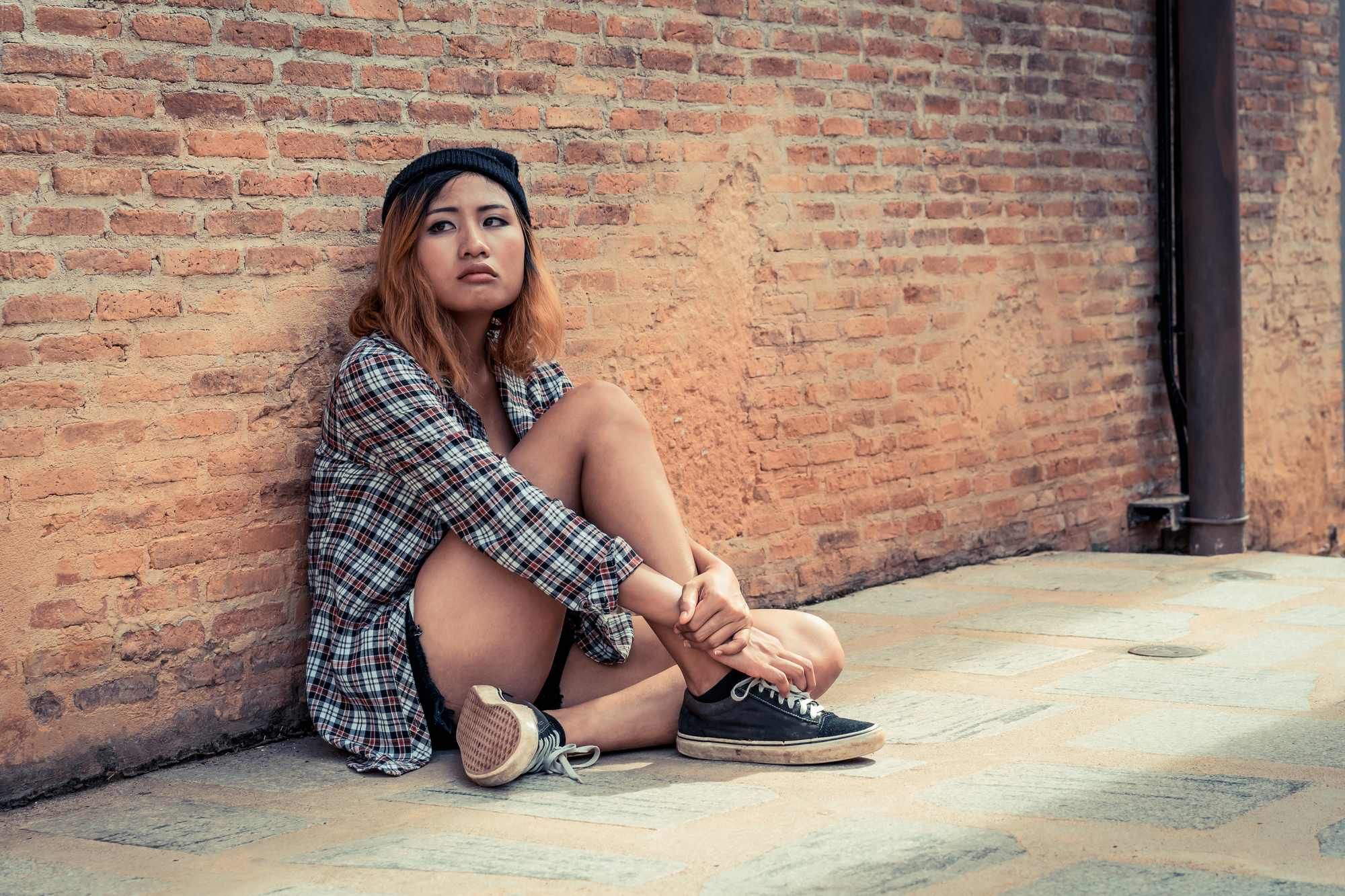 Depressed teen girl sits against a brick wall