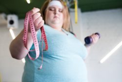 Obese woman holds tape measure in one hand and a weight in the other