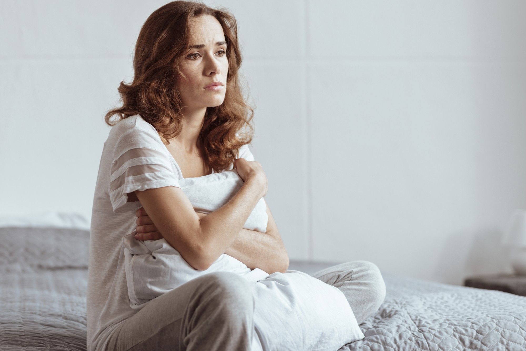 Serious woman sits and hugs pillow as she thinks