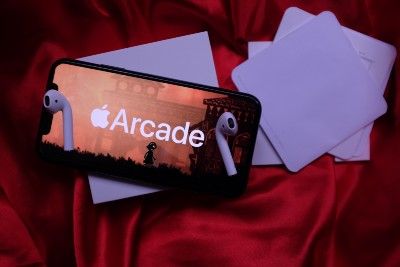 Apple Arcade is seen on an iPhone, with AirPods lying on top