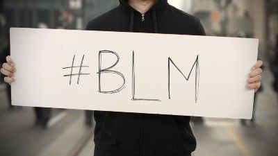 A protester in a black hoodie holds a "#BLM" sign - Black Lives Matter