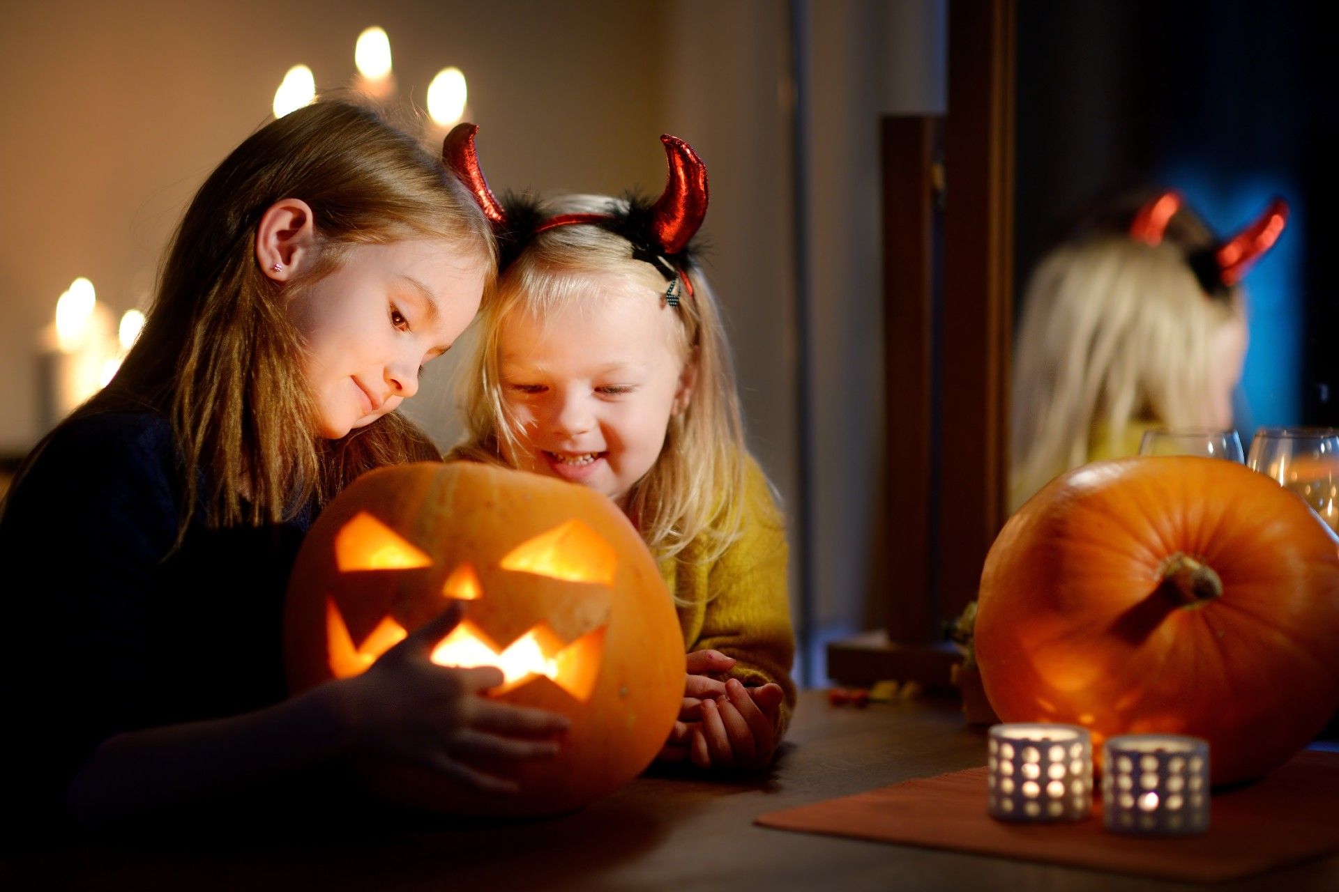 Two young girls carve light a jack-o-lantern, with candles in the background - safety tips on halloween