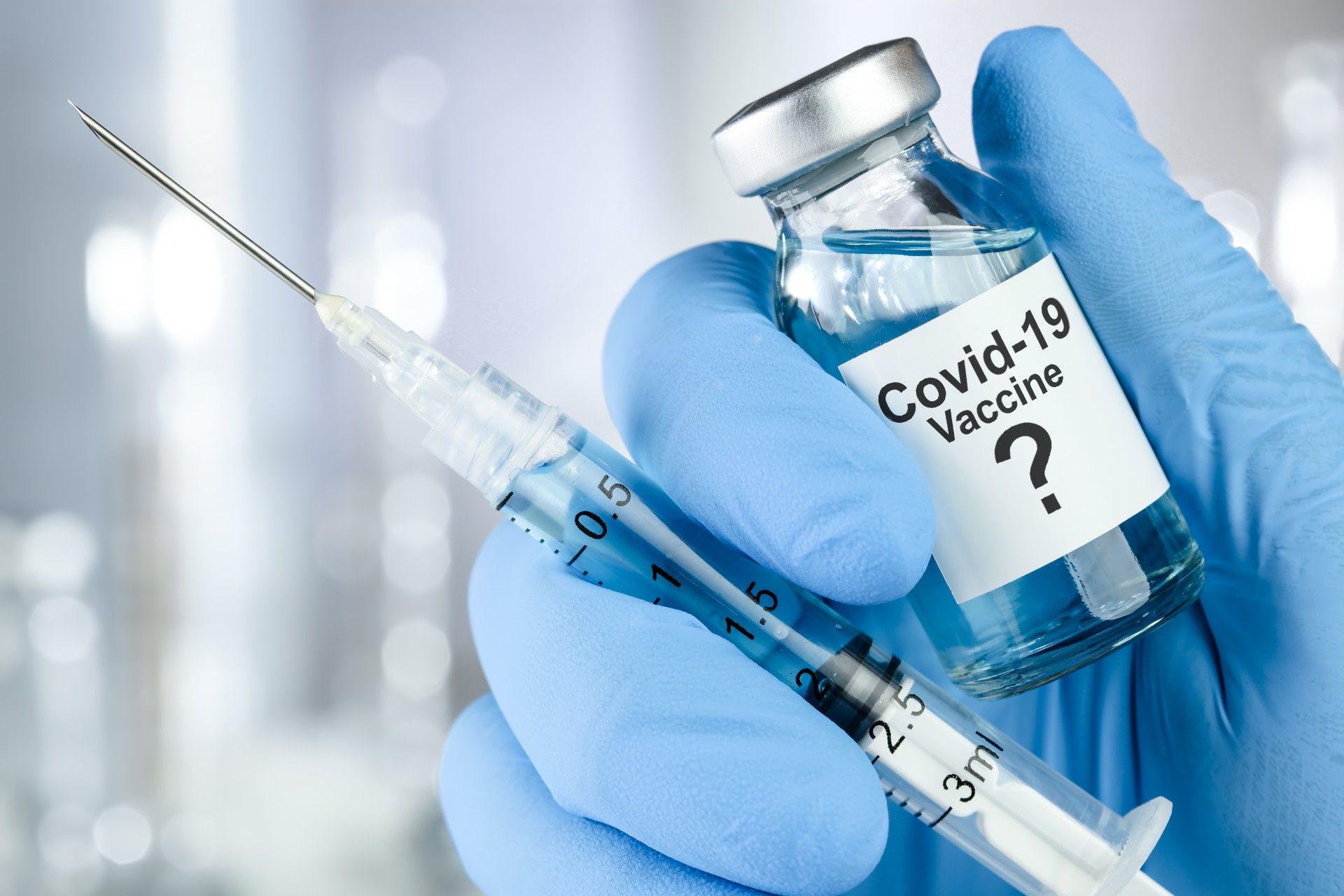 A blue-gloved hand holds a syringe and a vaccine bottle with a label that reads "Covid-19 Vaccine?" - coronavirus vaccine