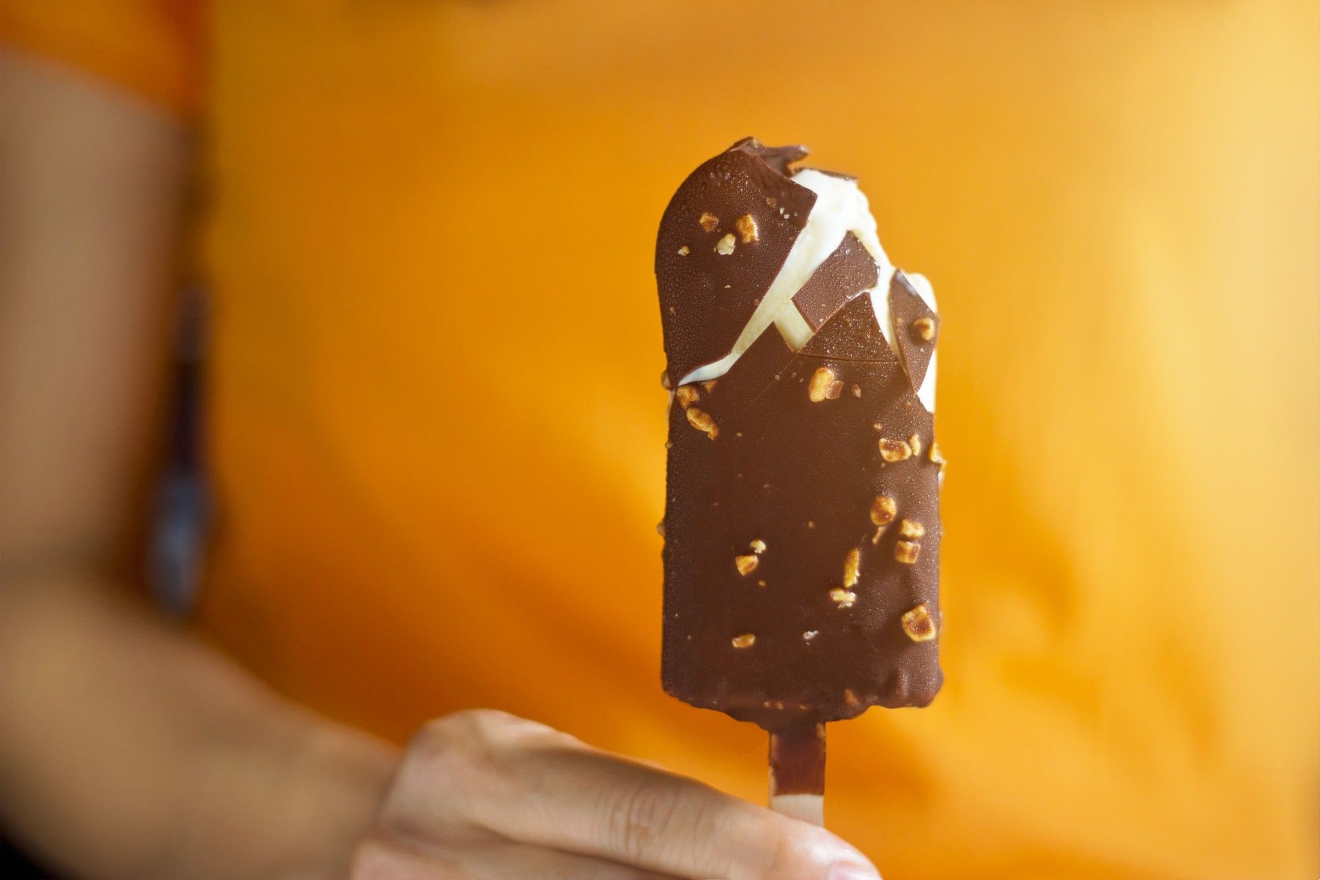 A person in a yellow shirt holds an ice cream bar dipped in chocolate and nuts - Whole Foods ice cream