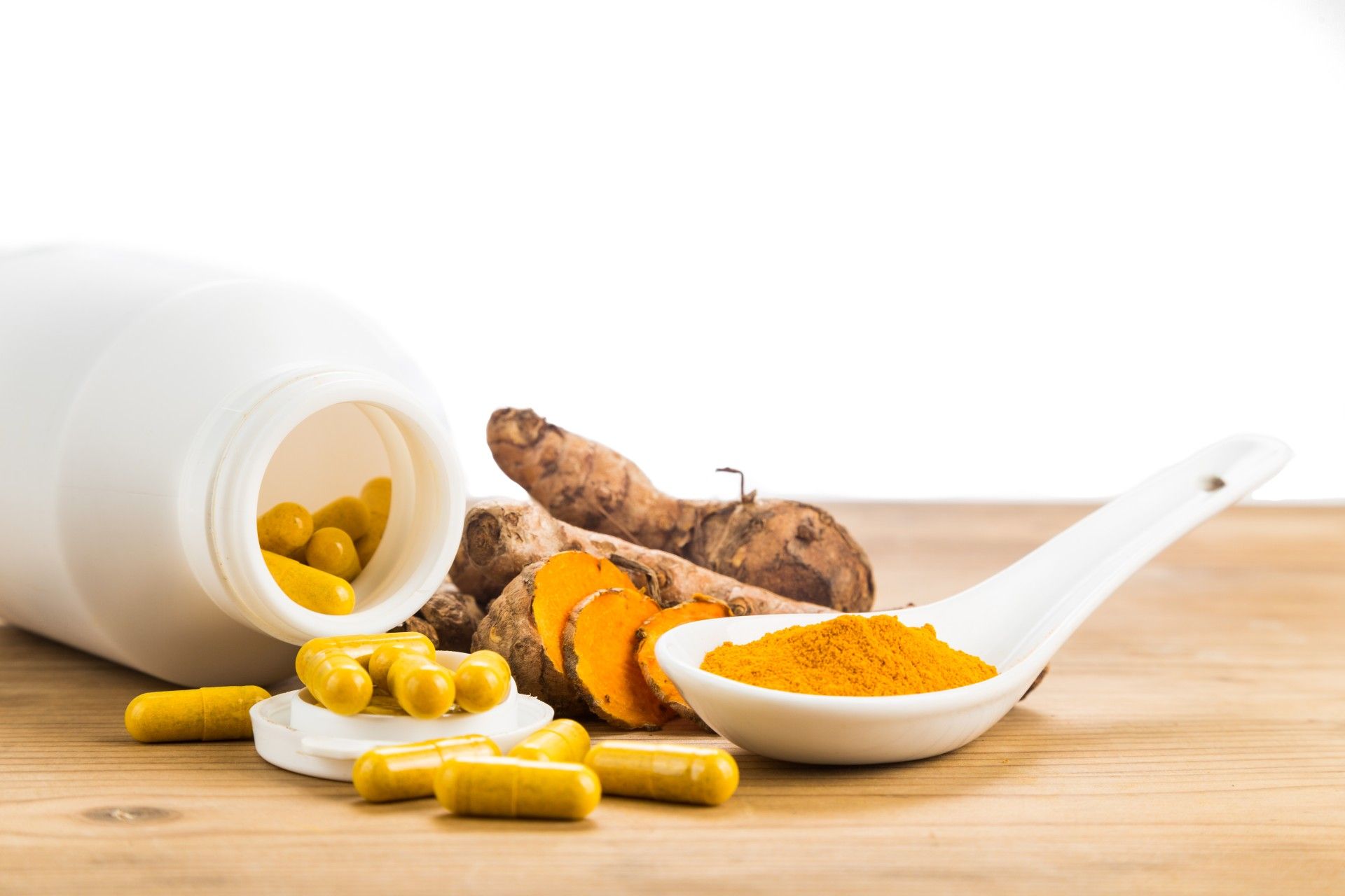 Powdered turmeric in a spoon next to whole turmeric and turmeric pills - pain relief