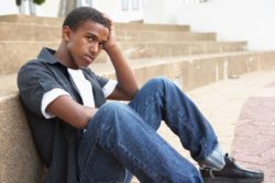 Unhappy teen male sits on steps outside