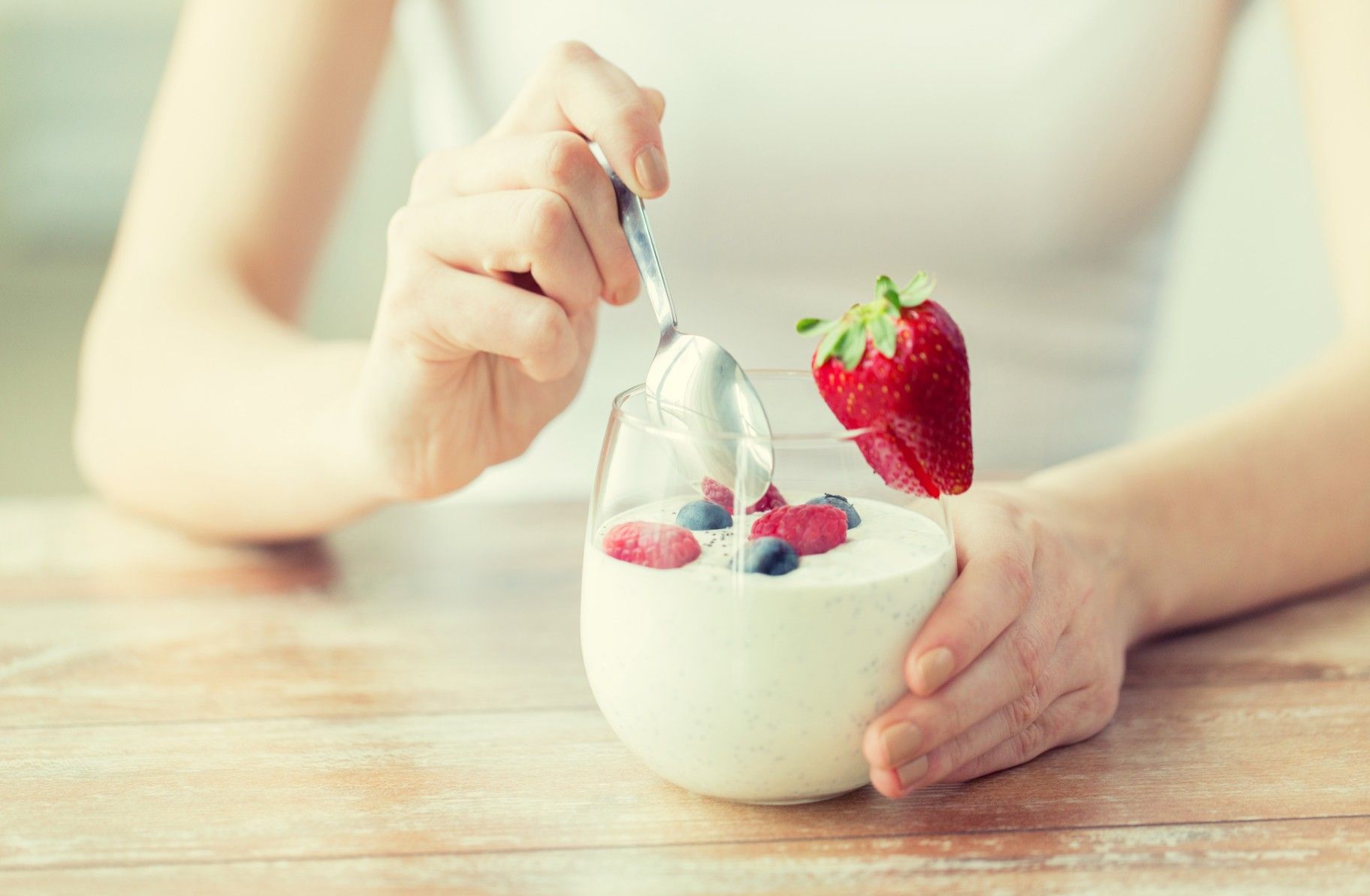 A woman's hands hold a glass of yogurt and fruit as she digs in a spoon - chobani greek yogurt